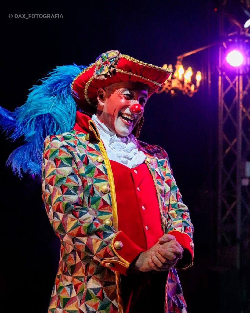 Payaso con maquillaje blanco y traje de muchos colores posa en el escenario.