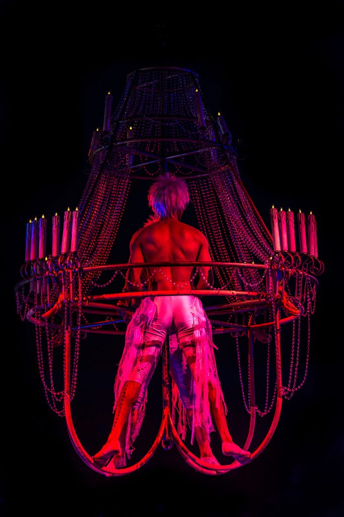 Artista posa dentro de una estructura metálica circular bajo una luz roja.