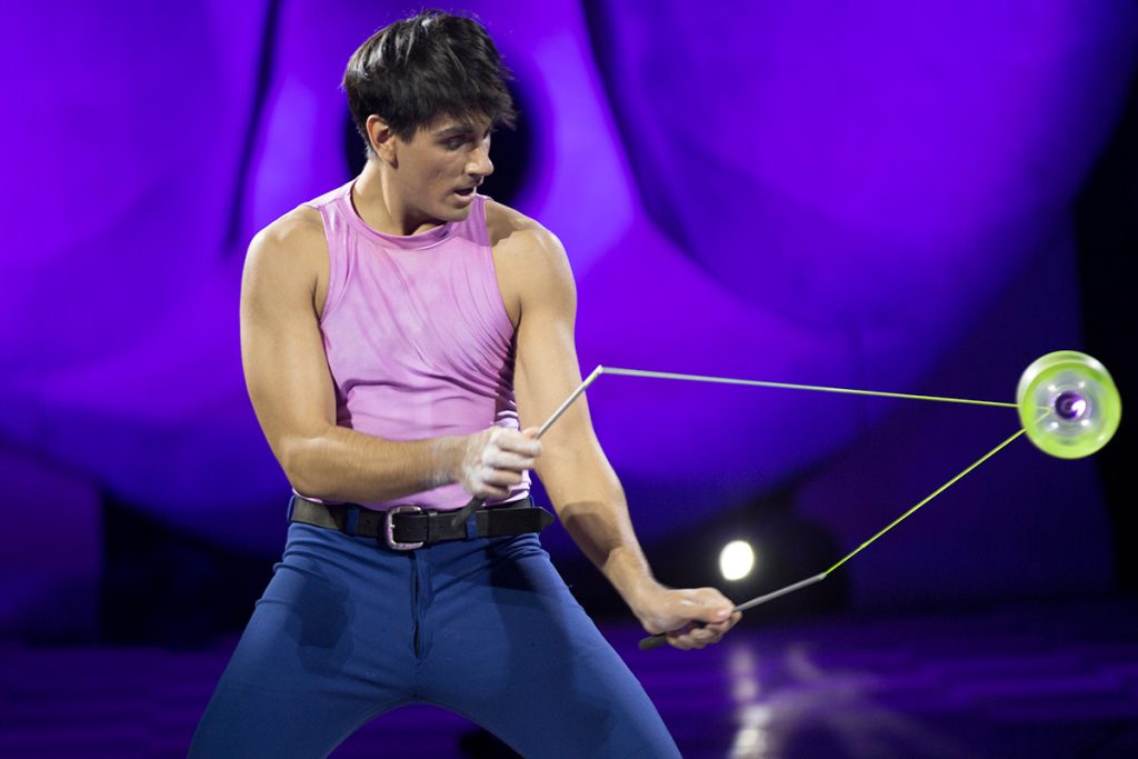 Artista de vestuario violeta actúa sentado bajo una iluminación púrpura.