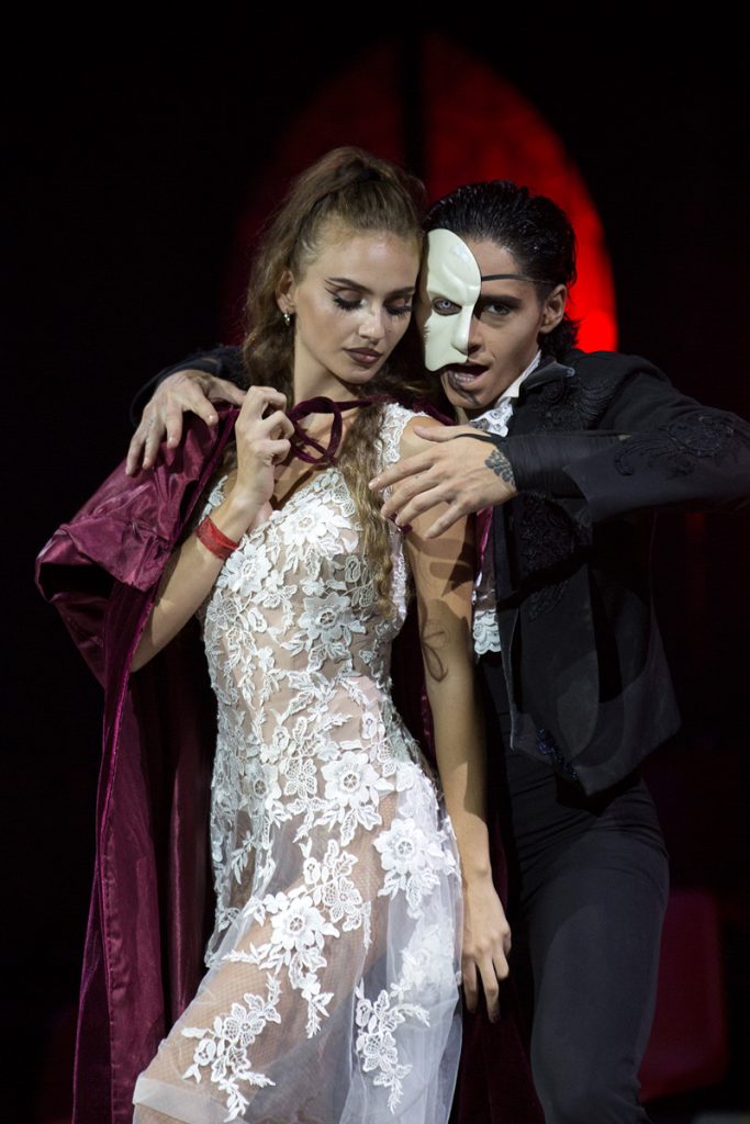 Una novia vestida de blanco aparece junto a un personaje de negro en una escena teatral de atmósfera gótica.
