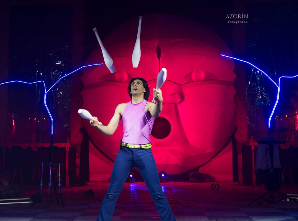 Dos artistas realizan una escena teatral delante de un gran círculo rojo iluminado.