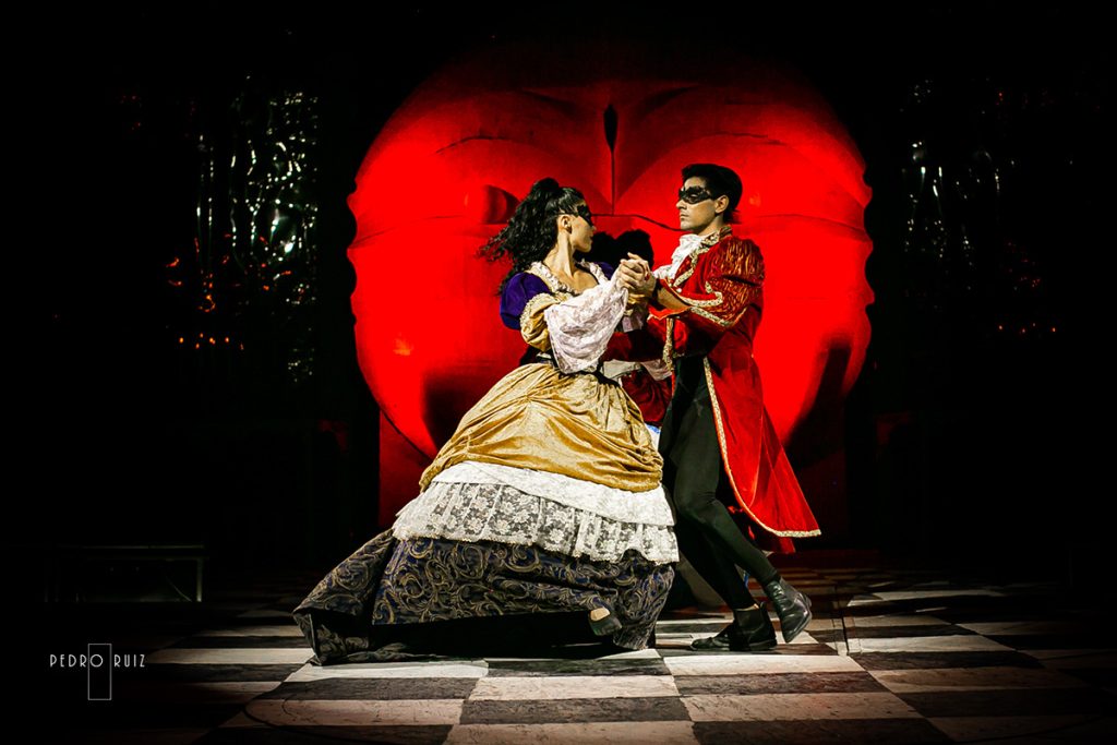 Dos intérpretes protagonizan una escena de baile teatral delante de un gran círculo rojo.