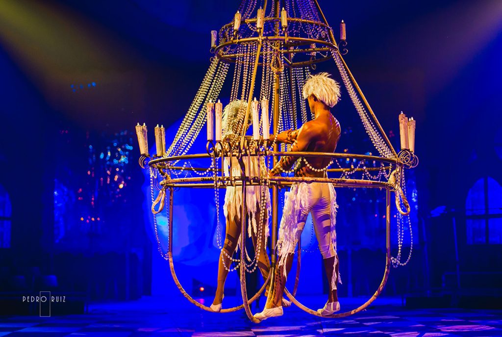 Estructura circular de circo con una artista en el escenario, iluminada en azul y dorado.