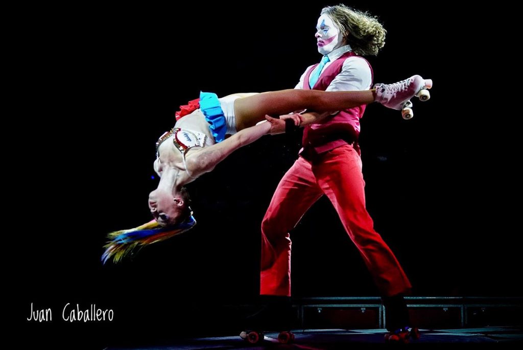 Un acróbata levanta a una artista vestida de blanco y rojo durante un número de circo.