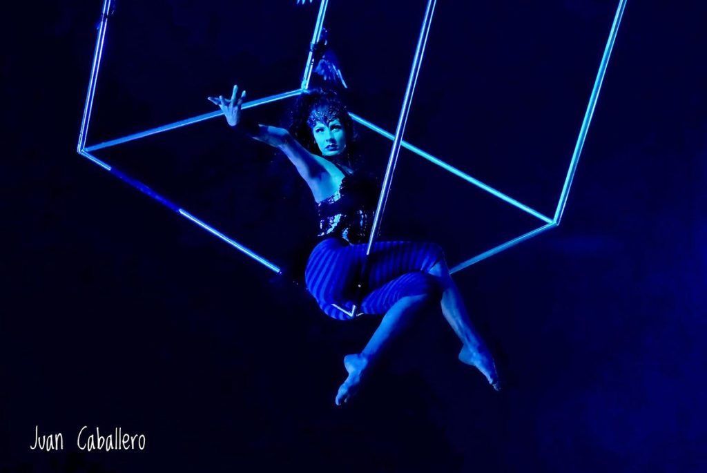 Artista realiza una figura acrobática en una estructura geométrica iluminada de azul.